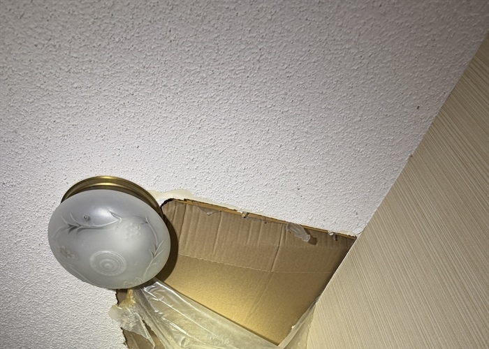 Pipe leak damage exposing a large opening in a popcorn ceiling near a light fixture