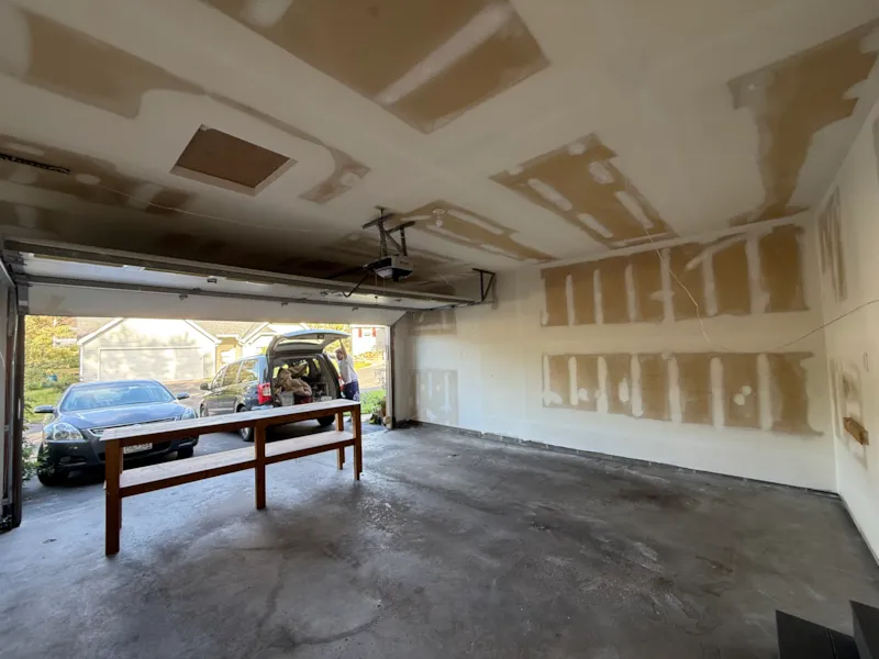Unfinished garage ceiling and side wall with drywall patches and open attic access