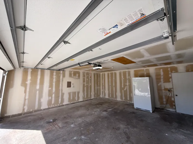 Garage walls with mudded drywall joints and a plywood-covered attic opening before finishing