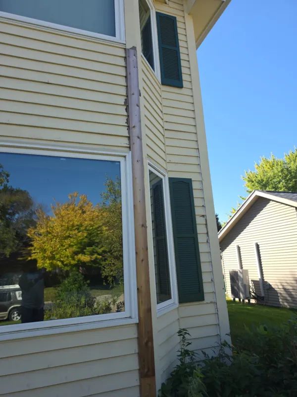 Bare wood trim board with peeling paint along a bay window on a Burnsville home